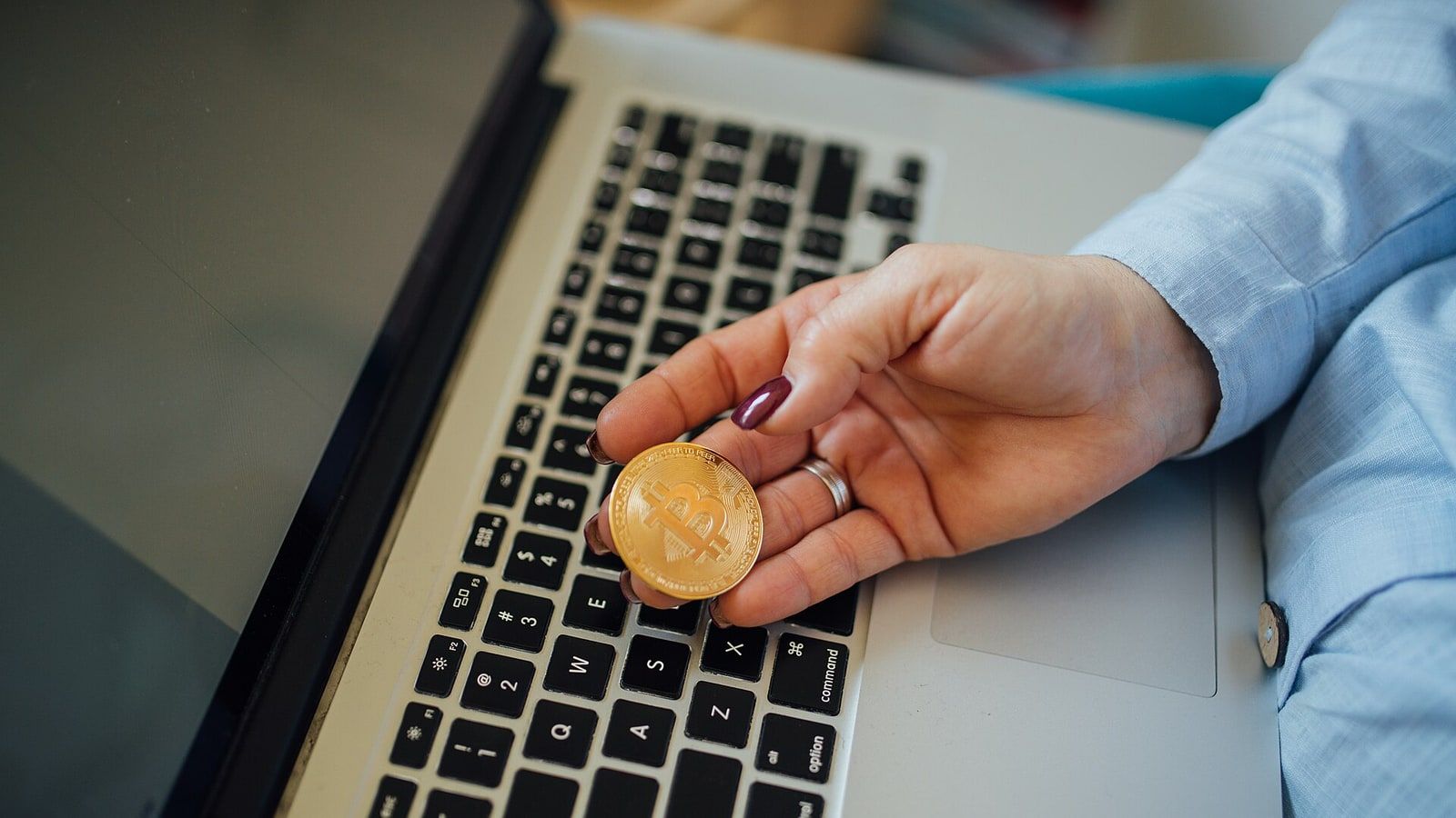 يد تحمل عملة بيتكوين ذهبية فوق لوحة مفاتيح حاسوب محمول